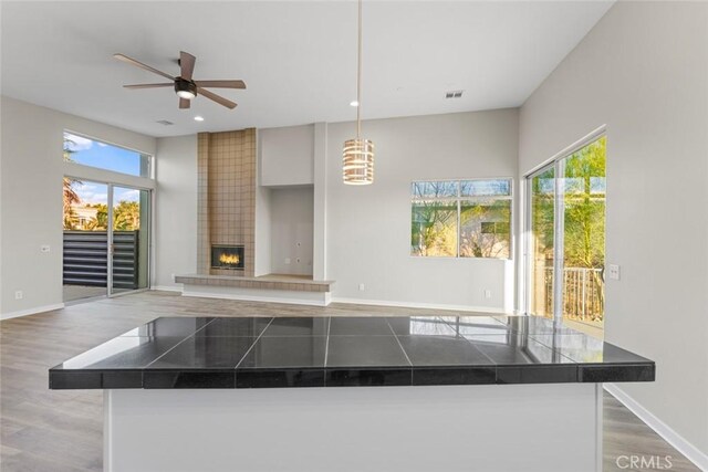 kitchen with plenty of natural light, wood-type flooring, a tile fireplace, and hanging light fixtures