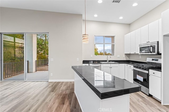 kitchen with sink, light hardwood / wood-style flooring, appliances with stainless steel finishes, hanging light fixtures, and white cabinets