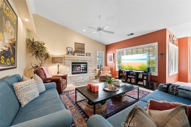 living room with vaulted ceiling, a stone fireplace, and ceiling fan