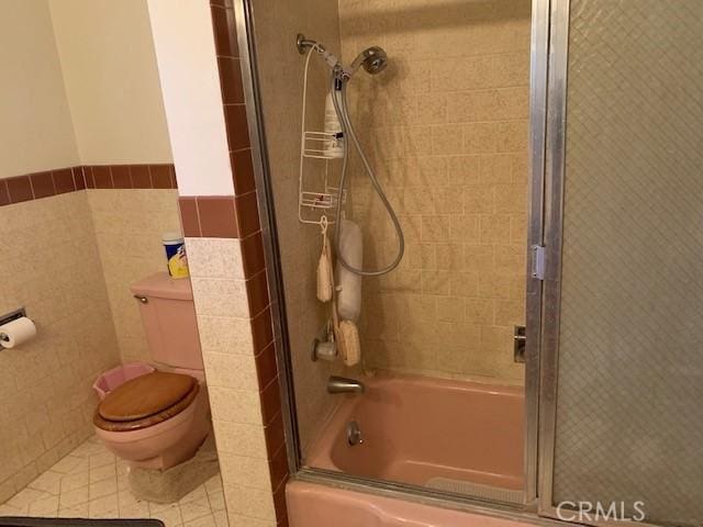 bathroom featuring tile patterned flooring, tile walls, shower / bath combination with glass door, and toilet