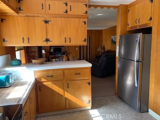 kitchen with tile countertops, stainless steel refrigerator, and wood walls