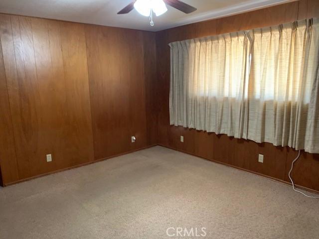 empty room featuring ceiling fan, light colored carpet, and wooden walls