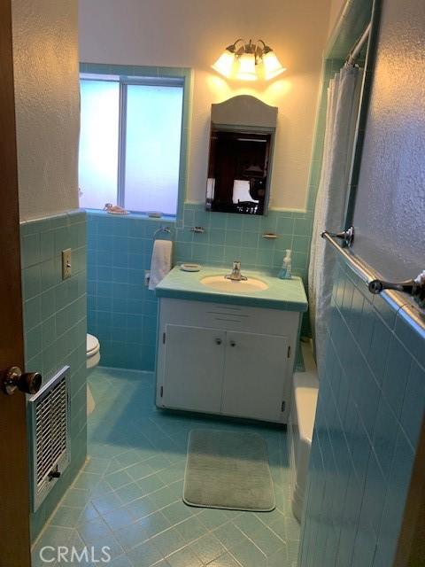 bathroom with tile patterned flooring, vanity, toilet, and tile walls