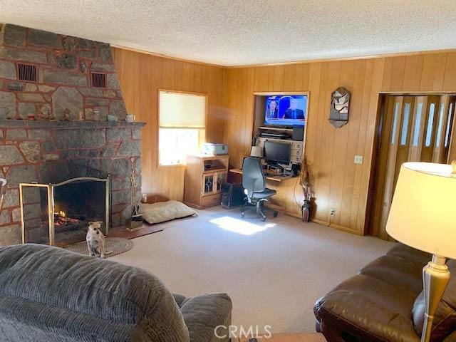 carpeted living room with a stone fireplace, wooden walls, and a textured ceiling