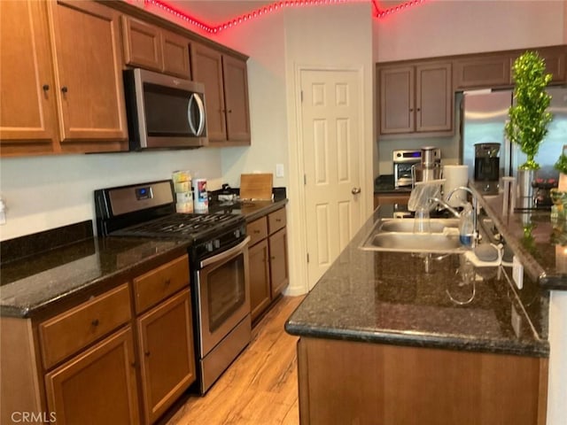 kitchen with dark stone countertops, stainless steel appliances, sink, and light wood-type flooring