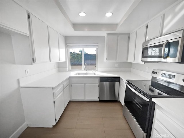 kitchen with light tile patterned flooring, a raised ceiling, white cabinetry, sink, and stainless steel appliances