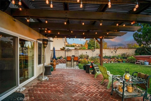 patio terrace at dusk with a yard, a pergola, and an outdoor bar