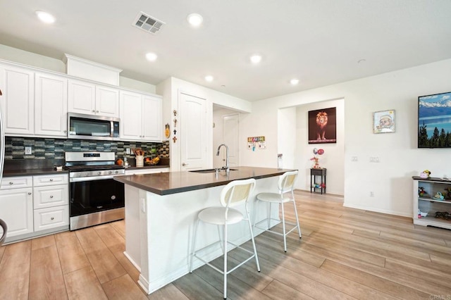 kitchen with a kitchen bar, white cabinetry, tasteful backsplash, an island with sink, and stainless steel appliances