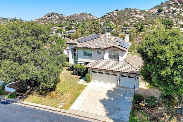 view of front of home with a garage, a mountain view, a front lawn, and solar panels