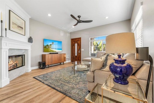 living room with a premium fireplace, ceiling fan, and light wood-type flooring