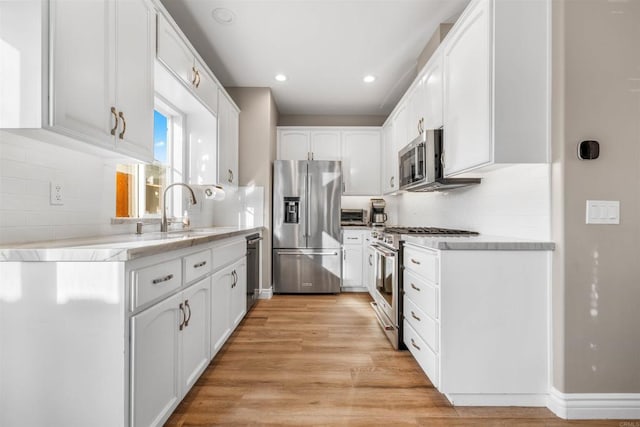 kitchen featuring sink, appliances with stainless steel finishes, white cabinets, decorative backsplash, and light wood-type flooring