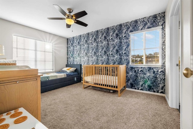 bedroom with a nursery area, ceiling fan, and carpet flooring