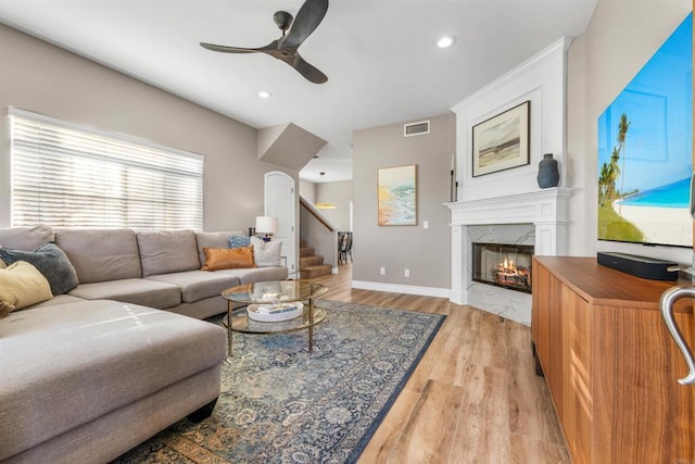 living room with a fireplace, ceiling fan, and light wood-type flooring