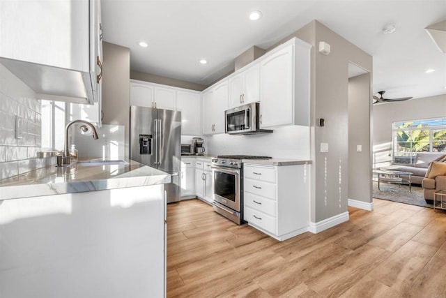 kitchen featuring sink, white cabinetry, light wood-type flooring, stainless steel appliances, and backsplash