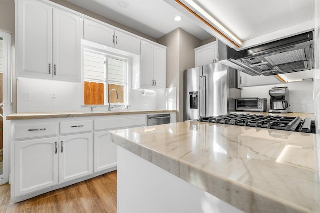 kitchen with white cabinetry, stainless steel appliances, light stone countertops, exhaust hood, and light wood-type flooring