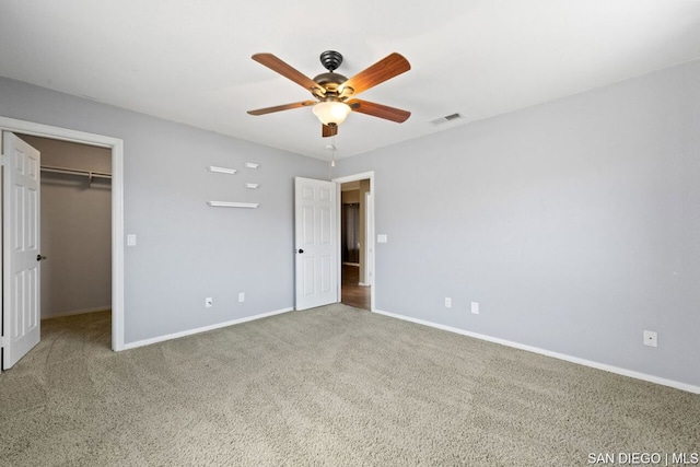 unfurnished bedroom featuring a spacious closet, a closet, ceiling fan, and carpet