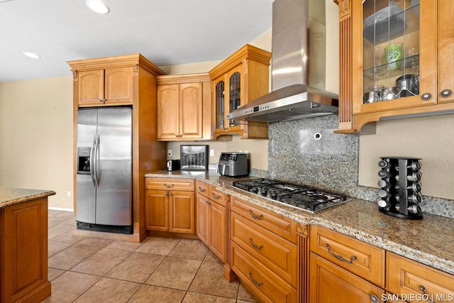 kitchen featuring light stone countertops, appliances with stainless steel finishes, light tile patterned floors, and wall chimney exhaust hood