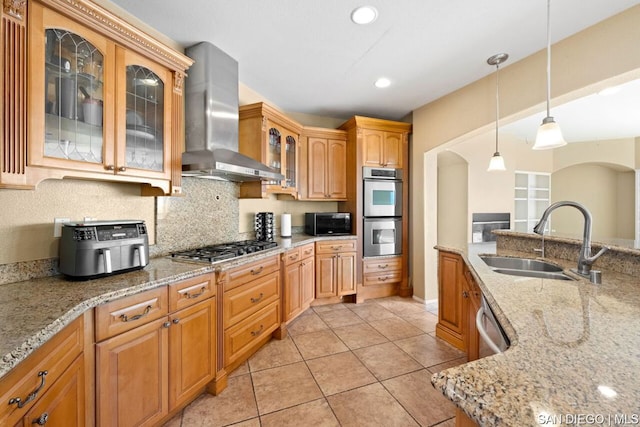 kitchen with sink, appliances with stainless steel finishes, light stone counters, decorative light fixtures, and wall chimney exhaust hood