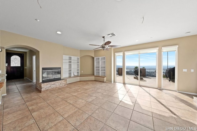 unfurnished living room featuring built in shelves, ceiling fan, a water view, and light tile patterned floors