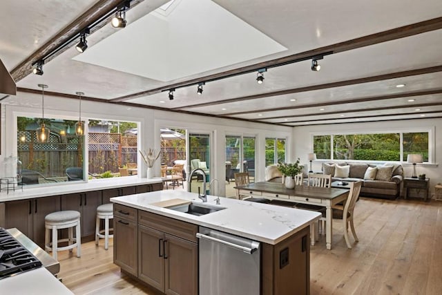 kitchen with sink, hanging light fixtures, a center island with sink, stainless steel dishwasher, and light wood-type flooring