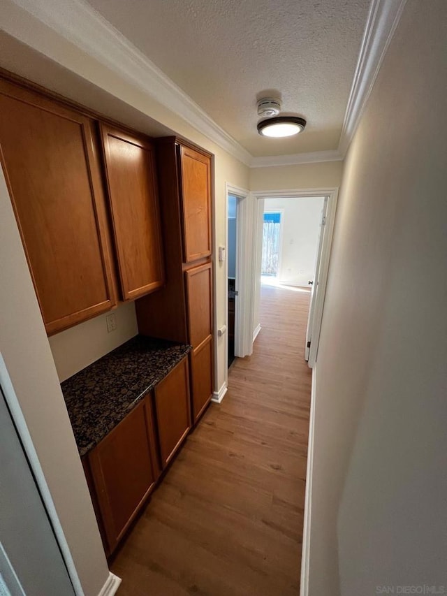 hall with light hardwood / wood-style flooring, ornamental molding, and a textured ceiling