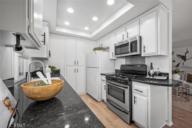 kitchen featuring stainless steel appliances, a raised ceiling, light wood-type flooring, and white cabinets