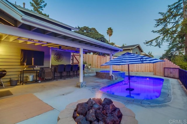 pool at dusk with an in ground hot tub, exterior bar, and a patio area