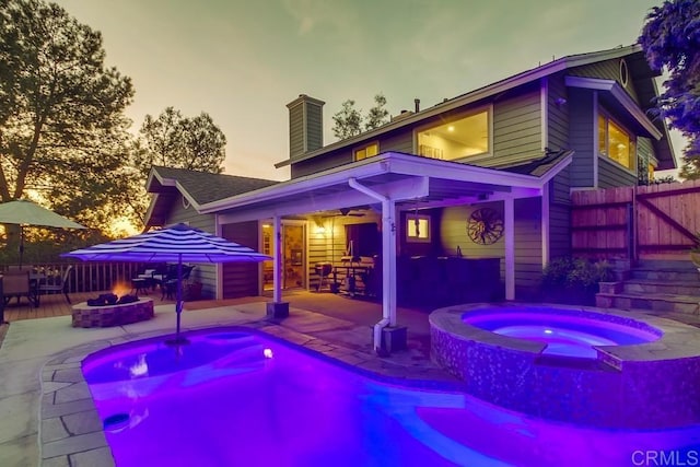 pool at dusk featuring a patio area, an in ground hot tub, ceiling fan, and an outdoor fire pit