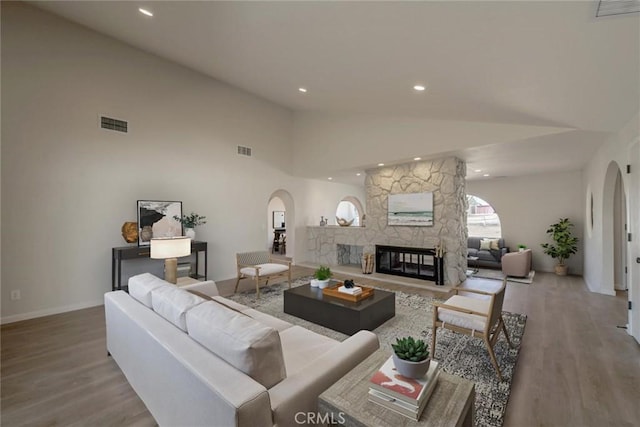 living room featuring a stone fireplace, high vaulted ceiling, and light wood-type flooring