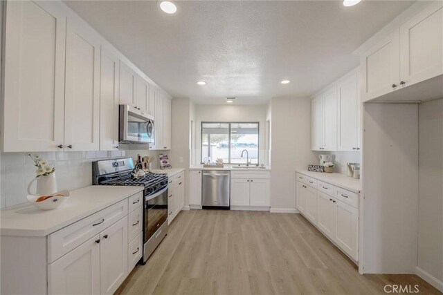 kitchen with stainless steel appliances, light hardwood / wood-style floors, sink, and white cabinets