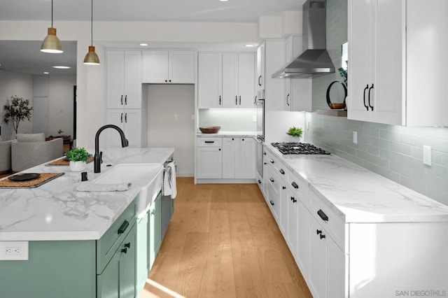 kitchen with white cabinetry, light stone counters, hanging light fixtures, and wall chimney range hood