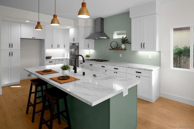 kitchen featuring white cabinetry, a kitchen island with sink, and wall chimney range hood