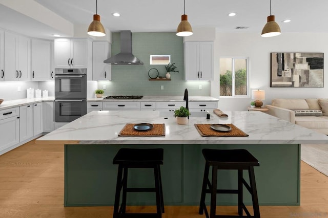 kitchen with stainless steel appliances, a kitchen island, wall chimney range hood, and white cabinets