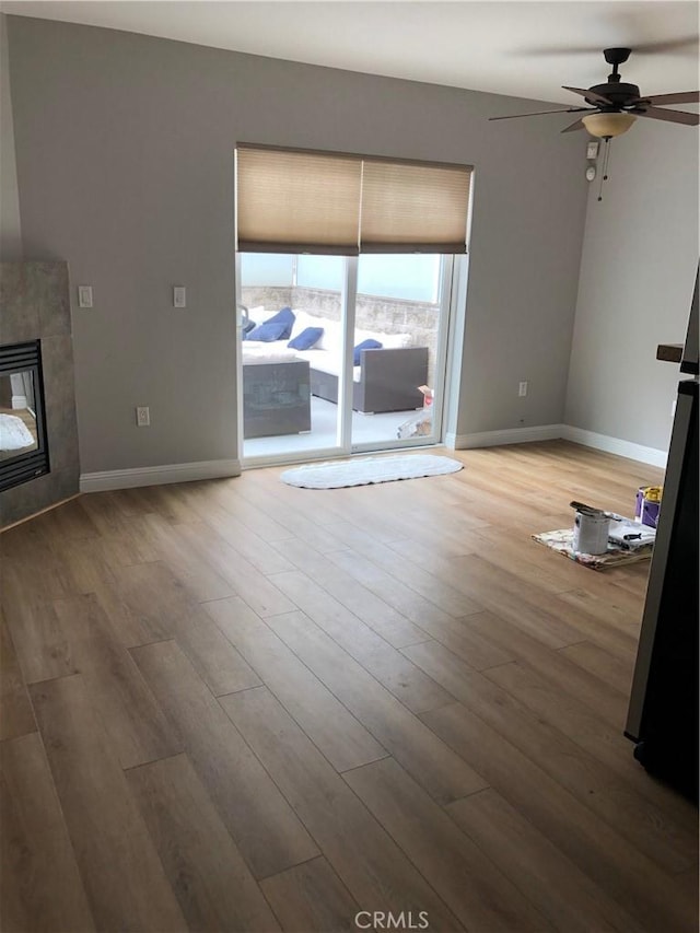 unfurnished living room featuring ceiling fan, a tiled fireplace, and hardwood / wood-style floors