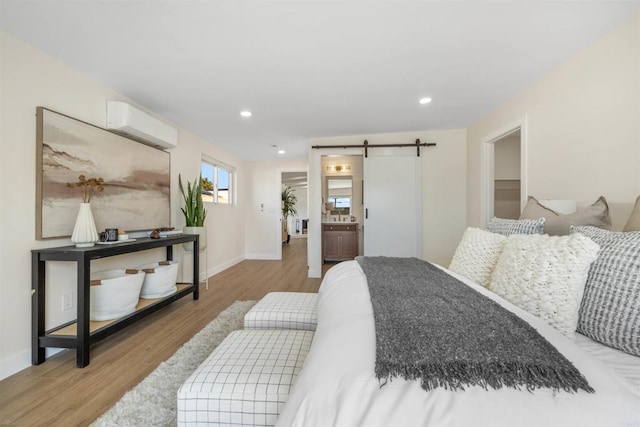 bedroom featuring a barn door, a wall mounted AC, and light hardwood / wood-style floors