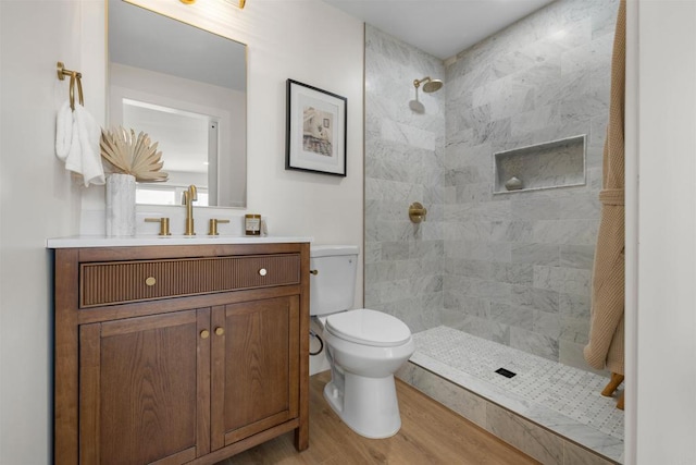 bathroom featuring hardwood / wood-style flooring, tiled shower, vanity, and toilet