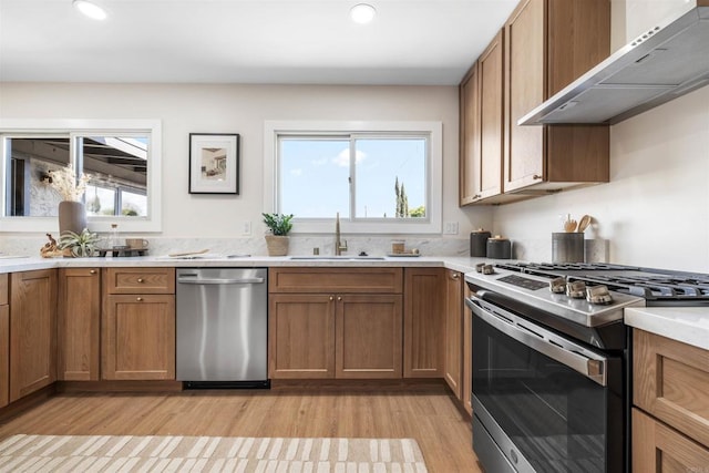 kitchen with a healthy amount of sunlight, sink, wall chimney exhaust hood, and appliances with stainless steel finishes