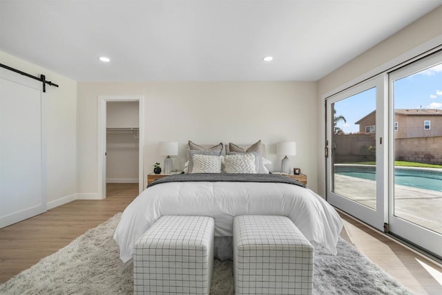 bedroom with a walk in closet, a barn door, light hardwood / wood-style floors, and access to outside