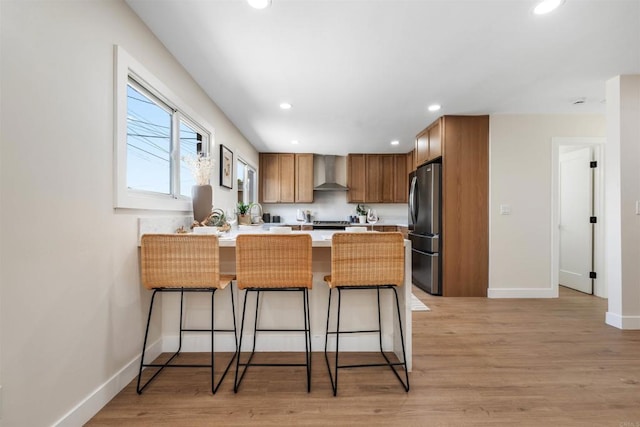 kitchen with a breakfast bar, stainless steel fridge, kitchen peninsula, light wood-type flooring, and wall chimney exhaust hood