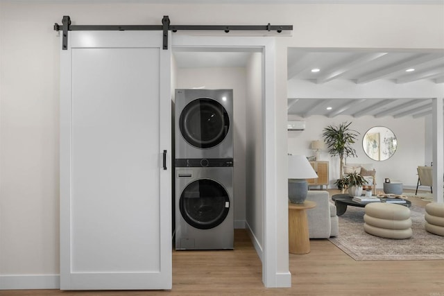 laundry area with stacked washing maching and dryer, a barn door, and light wood-type flooring