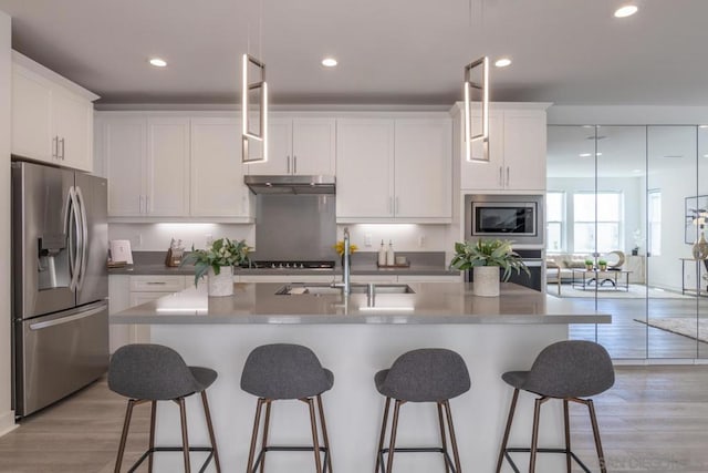 kitchen featuring appliances with stainless steel finishes, pendant lighting, sink, white cabinets, and a kitchen island with sink