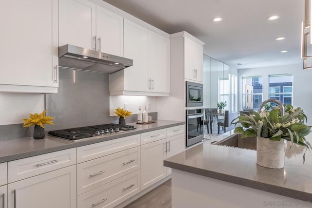 kitchen with white cabinetry, light wood-type flooring, dark stone counters, and appliances with stainless steel finishes