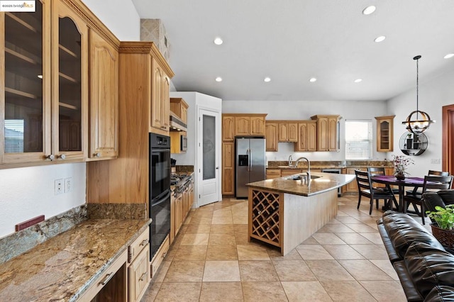 kitchen with dark stone countertops, hanging light fixtures, a kitchen island with sink, and appliances with stainless steel finishes