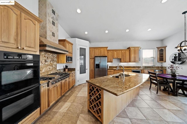 kitchen featuring pendant lighting, wall chimney range hood, sink, appliances with stainless steel finishes, and a center island with sink