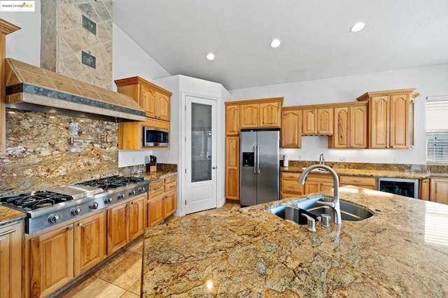 kitchen with light stone counters, stainless steel appliances, sink, and wall chimney range hood