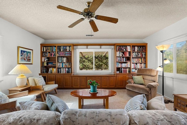 living area with ceiling fan, light colored carpet, and a textured ceiling