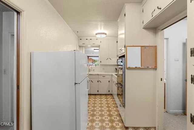 kitchen with white cabinetry, sink, and white fridge