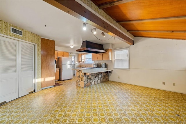 kitchen featuring a breakfast bar area, range hood, kitchen peninsula, beamed ceiling, and white fridge