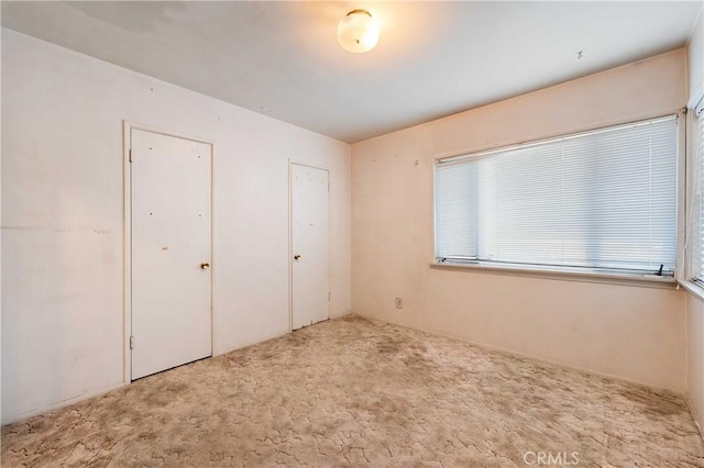 unfurnished bedroom featuring multiple closets and light colored carpet