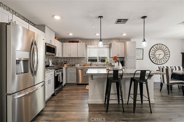 kitchen with decorative light fixtures, a center island, dark hardwood / wood-style flooring, stainless steel appliances, and light stone countertops